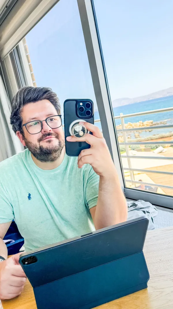 Benni im Sommer 2025 mit Brille und Bart am Fenster, vor sich ein Tablet