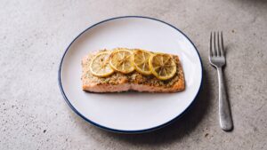 Lachs aus dem Airfryer low carb mit Zitronenscheiben und Würzpaste auf einem weißen Teller