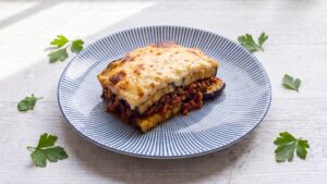 Moussaka low carb auf einem Teller mit sichtbaren Schichten aus Auberginen, Hackfleischsauce und cremiger Béchamel
